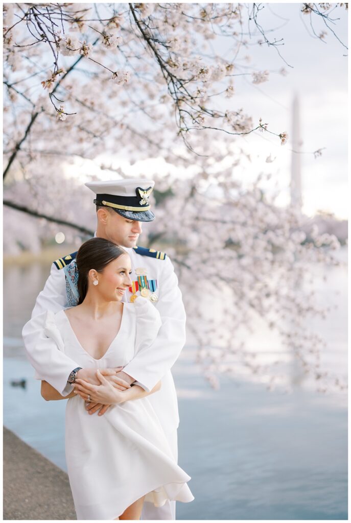 military service member and wife in front of the washington dc cherry blossoms and washington monument
